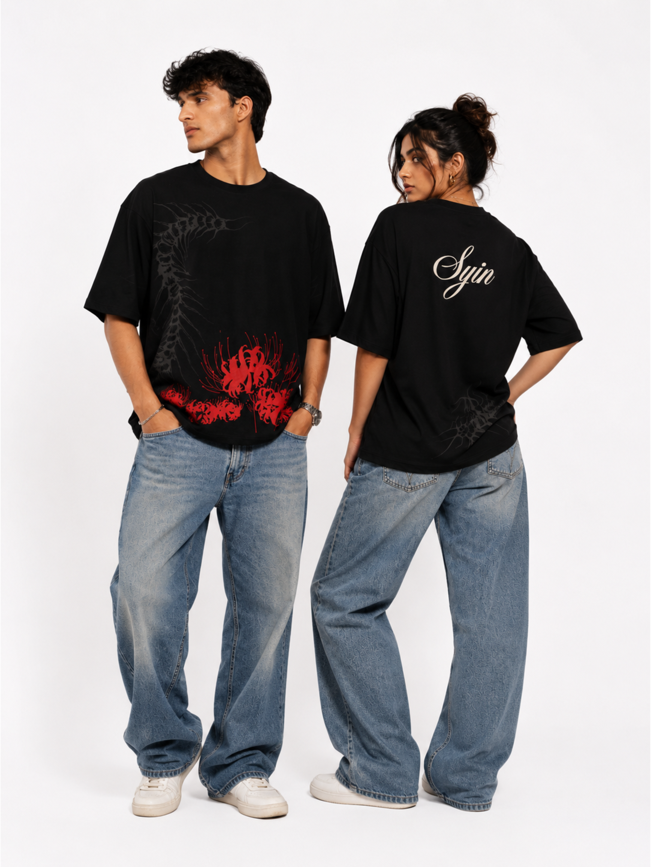 Male and female models showcasing the front and back of the Silken Spine premium oversized black T-shirt by SYIN & SYRAH featuring abstract spine artwork and red spider lily graphics.