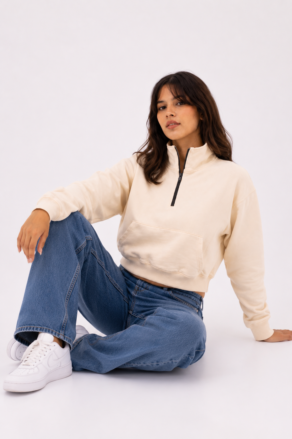 Female model seated wearing the Beige Crop Zipper, highlighting the heavyweight fleece, cropped silhouette, and quarter-zip neckline.