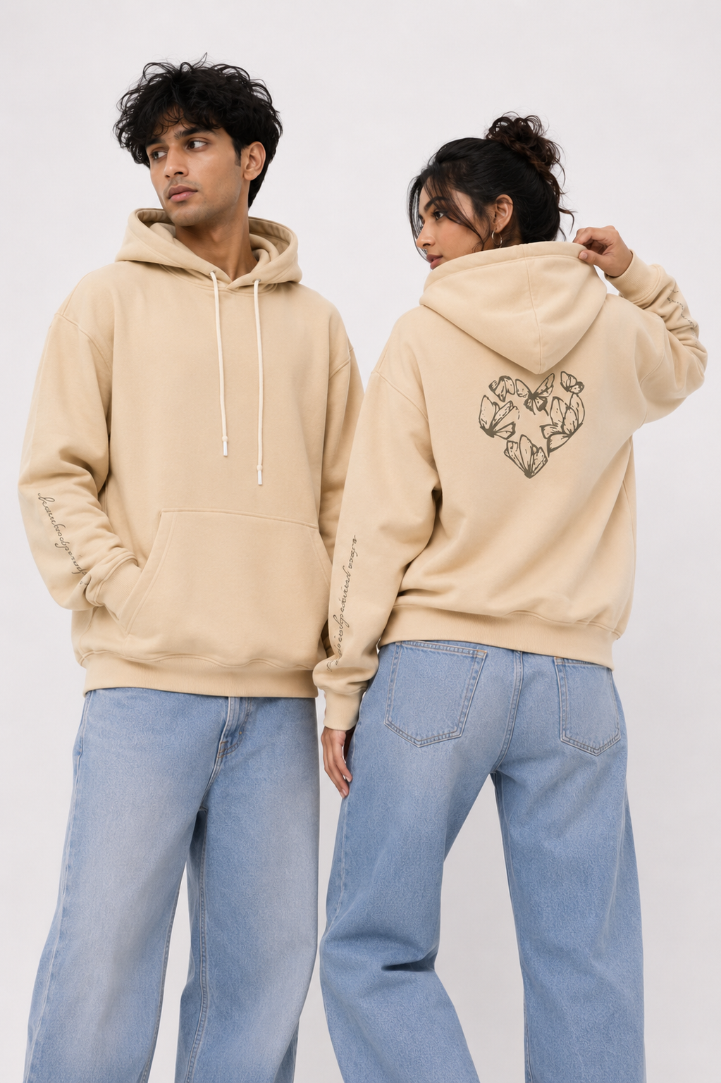 Front and back view of the Karmic Bloom oversized sand beige hoodie worn by male and female models featuring handwritten sleeve graphics and butterfly heart artwork.
