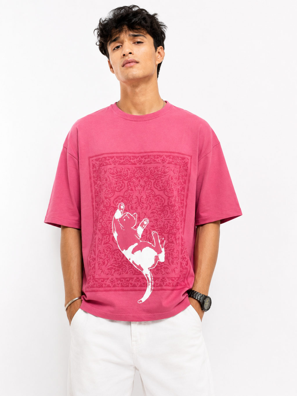 Male model wearing the Mid Air Myth oversized pink cotton T-shirt by SYIN & SYRAH featuring a minimalist falling cat graphic over Persian rug artwork in a premium studio portrait