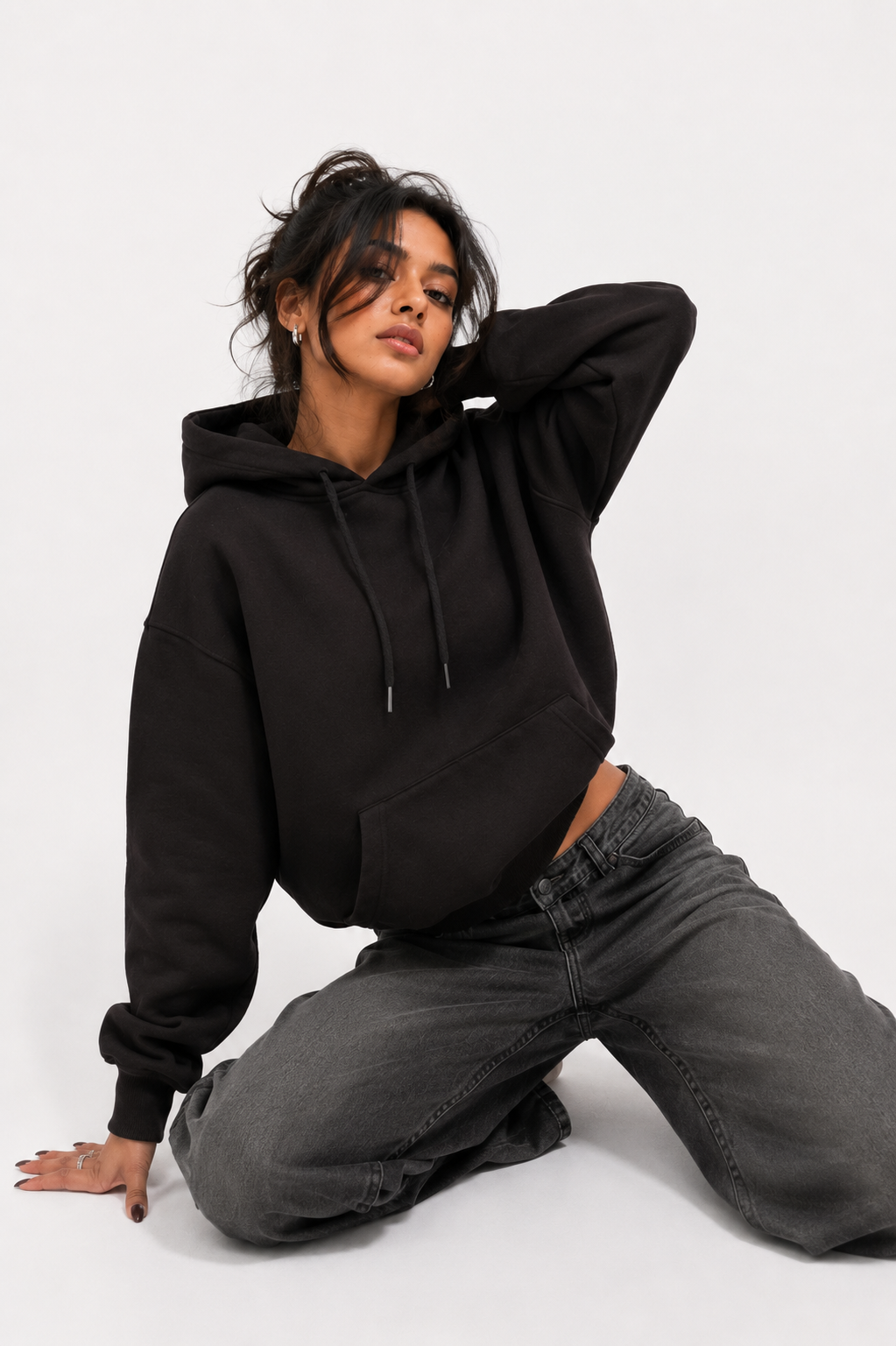 Female model wearing Midnight Lavender oversized black hoodie in a relaxed seated pose.
