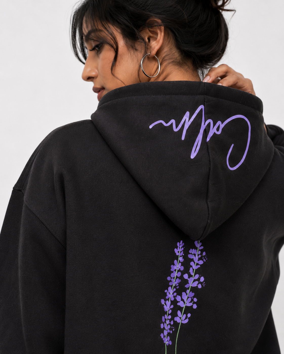Close-up of the Midnight Lavender oversized hoodie showcasing the lavender botanical artwork and signature script on the hood.