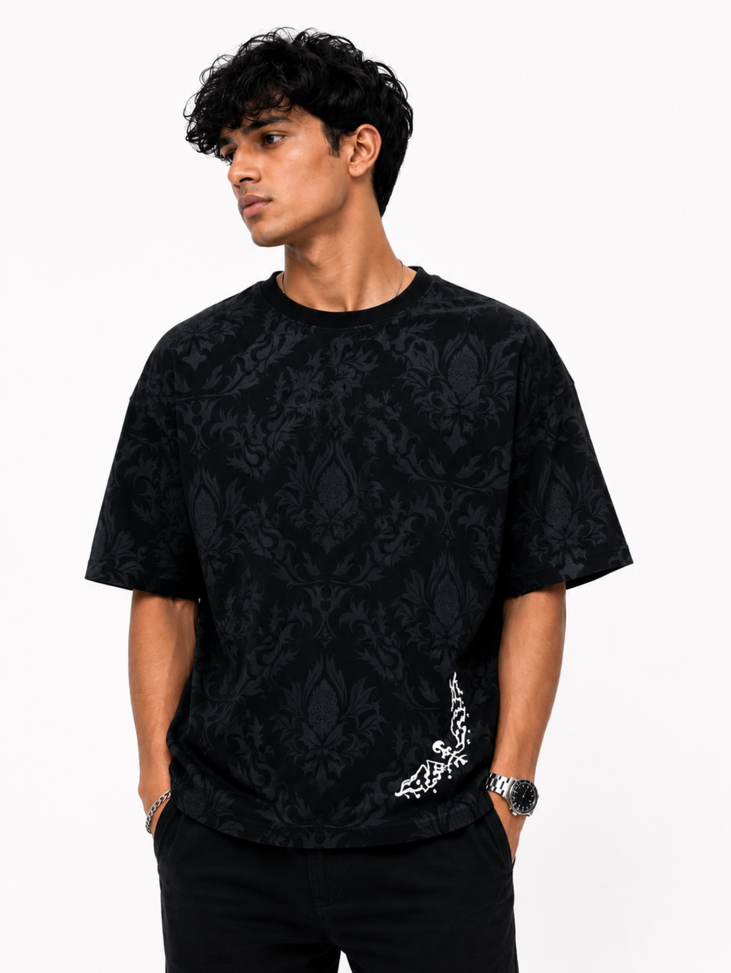 Male model wearing the Shadow Moth oversized black cotton graphic T-shirt by SYIN & SYRAH featuring an elegant tonal damask print with a minimalist white moth artwork in a premium studio portrait.