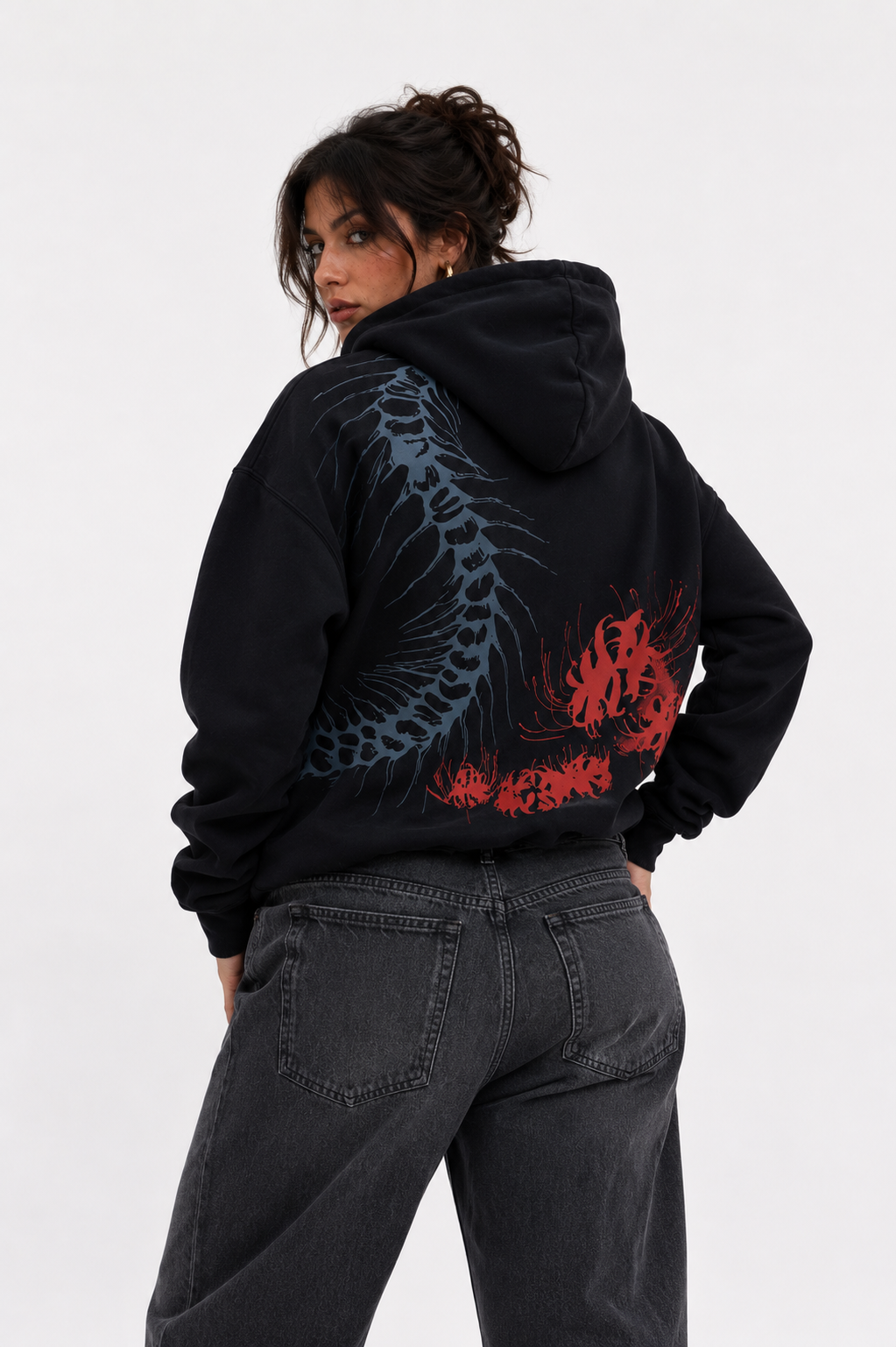 Female model wearing the Silken Spine oversized black hoodie from the back, displaying the anatomical spine and crimson spider lily artwork.