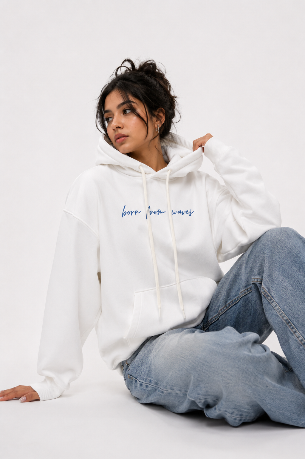 Female model wearing the Soul Born oversized white hoodie in a relaxed seated pose.