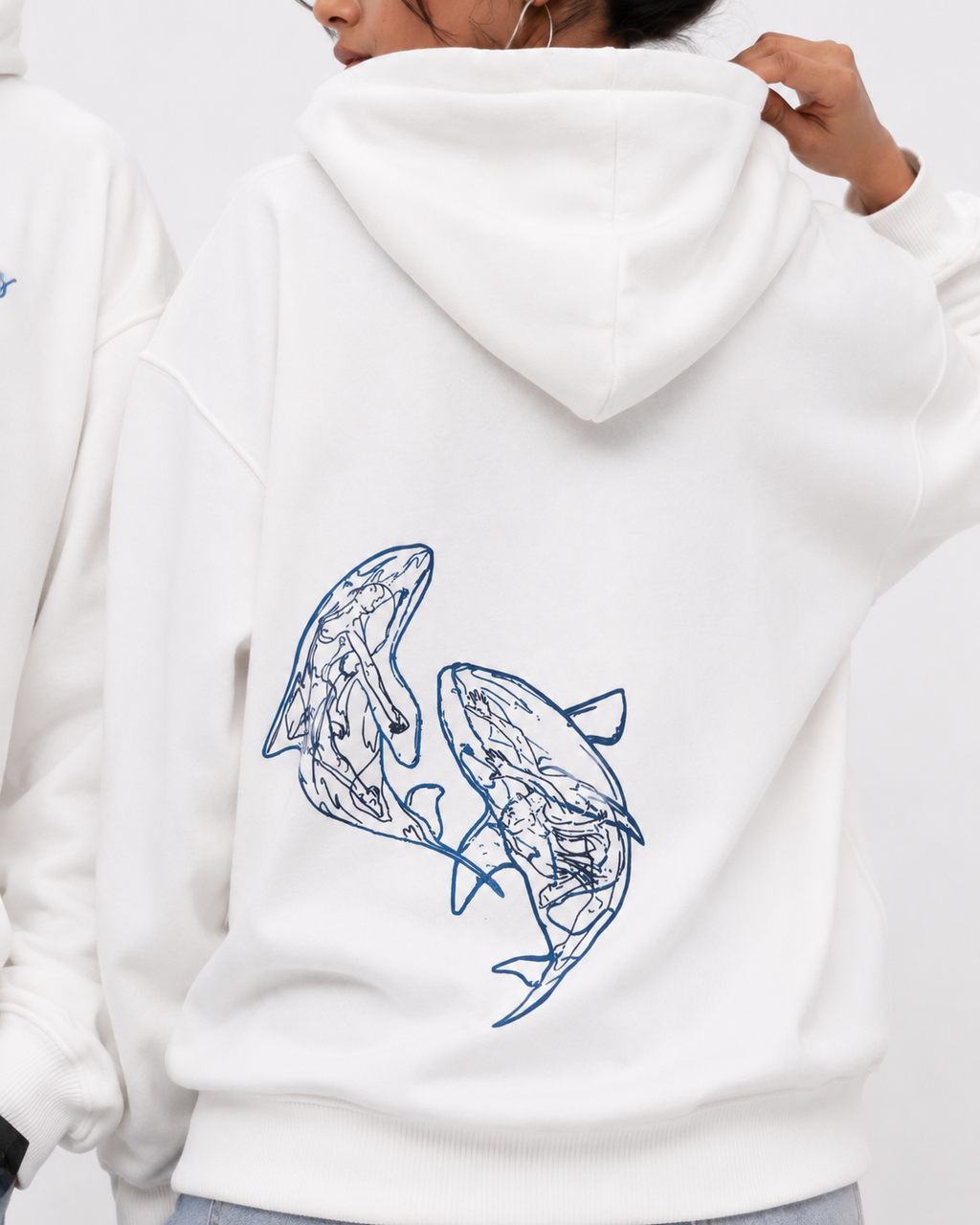 Close-up of the Soul Born oversized white hoodie featuring the blue twin whale artwork on the back.

