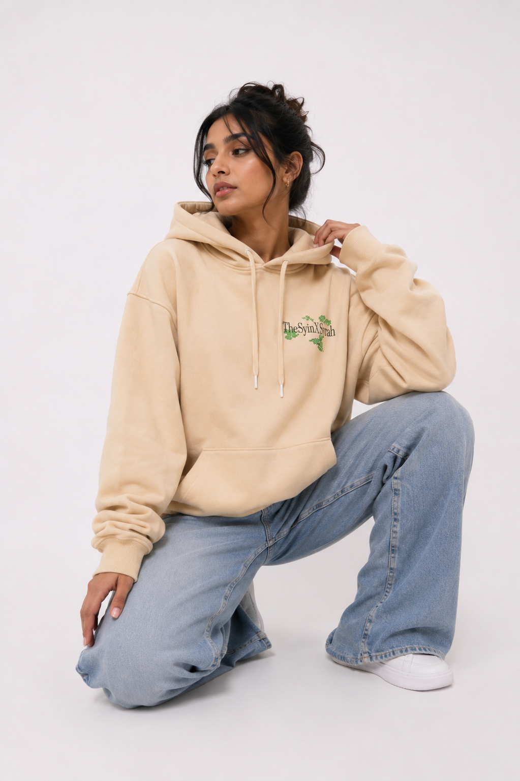 Female model wearing the Wild Grace oversized sand beige hoodie in a relaxed seated pose highlighting the premium oversized fit.
