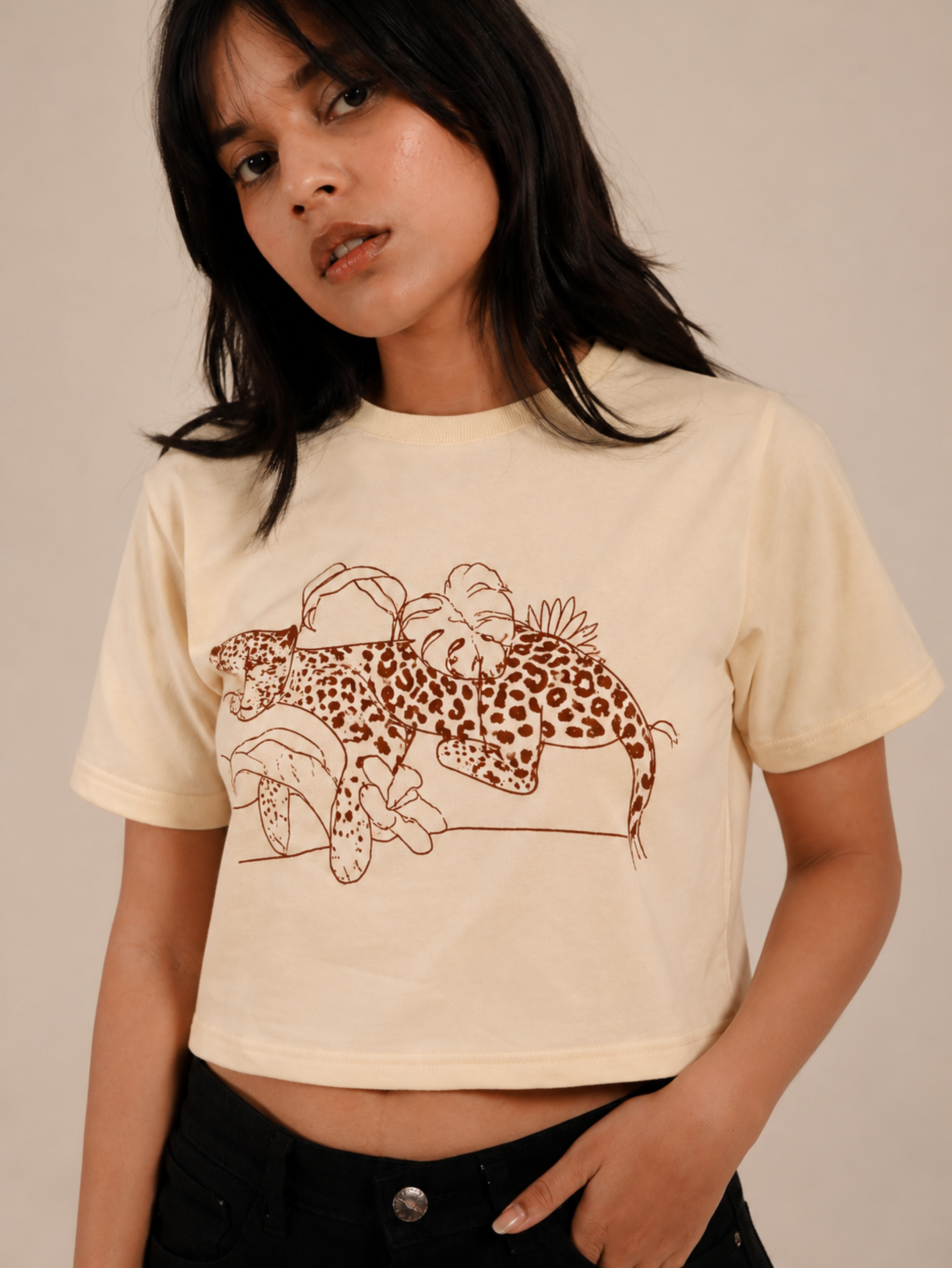 Female model wearing Wild Rest cream graphic crop top with black denim
