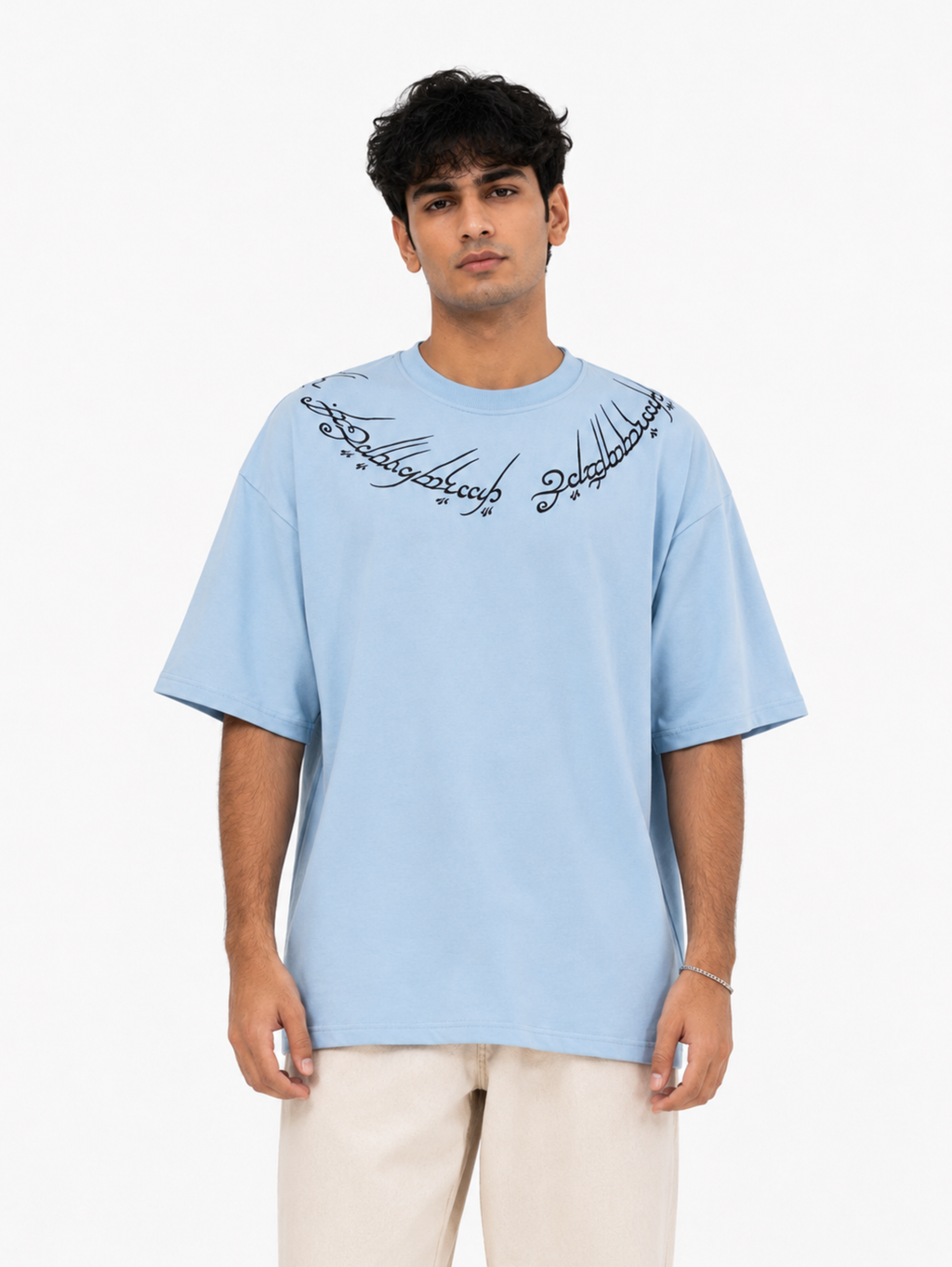 Male model wearing the Winged Curse oversized sky blue heavyweight cotton T-shirt by SYIN & SYRAH featuring gothic neckline typography in a clean white studio portrait.