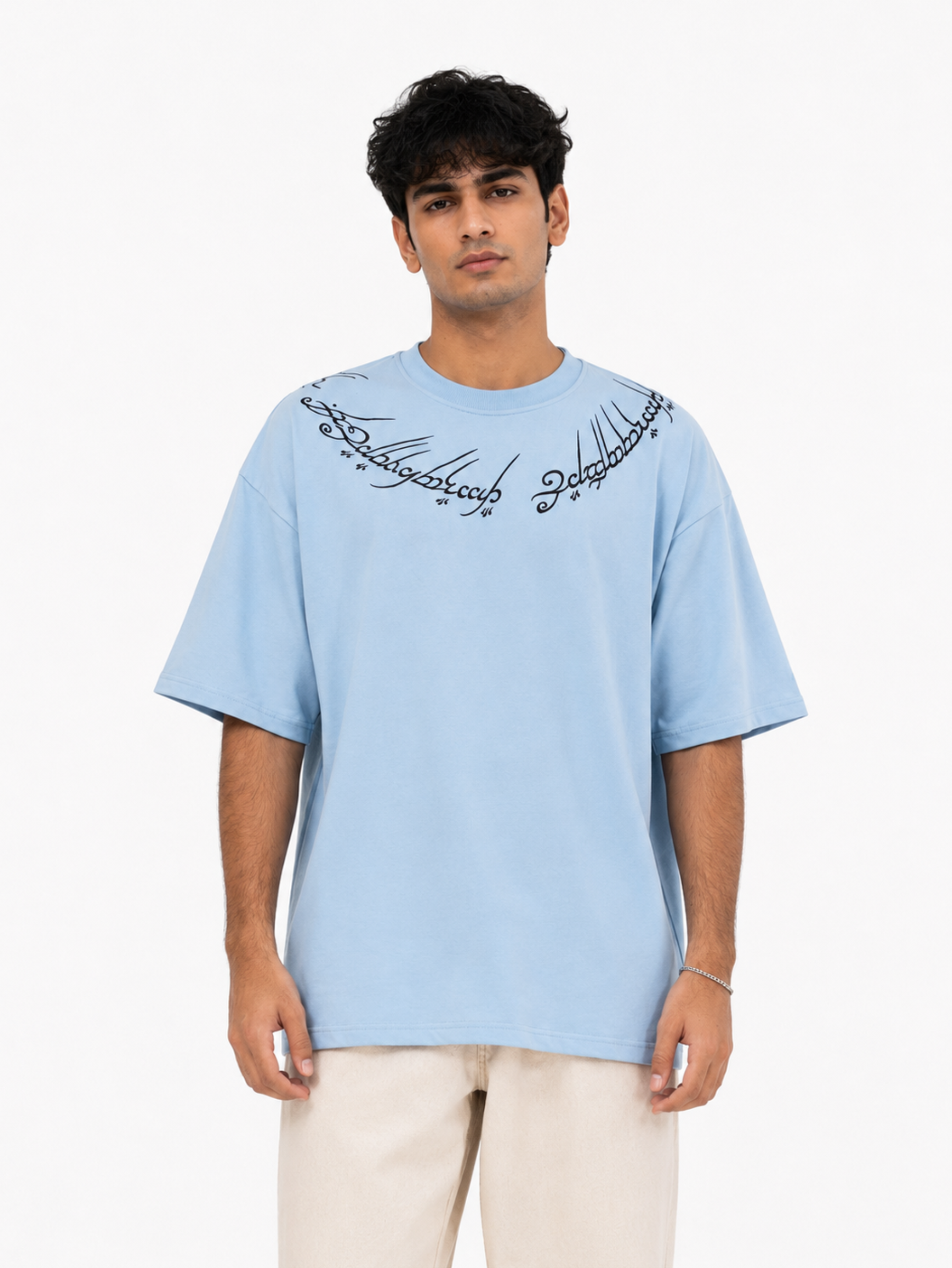 Male model wearing the Winged Curse oversized sky blue heavyweight cotton T-shirt by SYIN & SYRAH featuring gothic neckline typography in a clean white studio portrait.