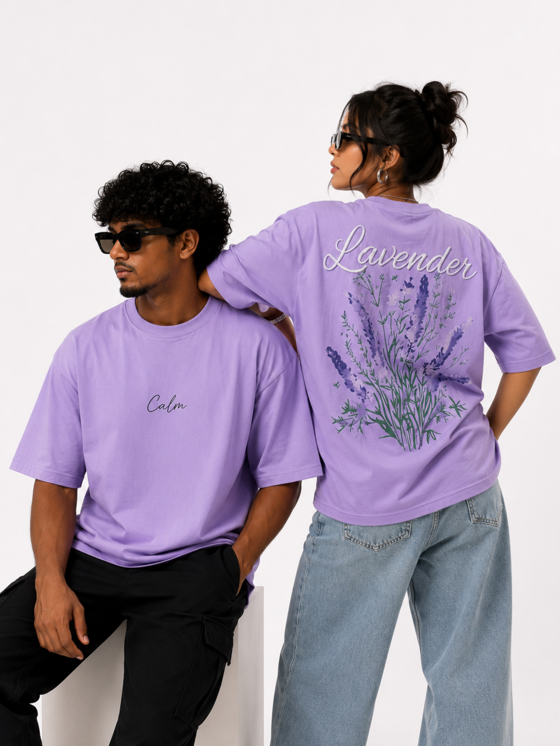 Male and female models wearing Still Bloom oversized lavender t-shirt showcasing minimalist front design and lavender floral artwork on the back