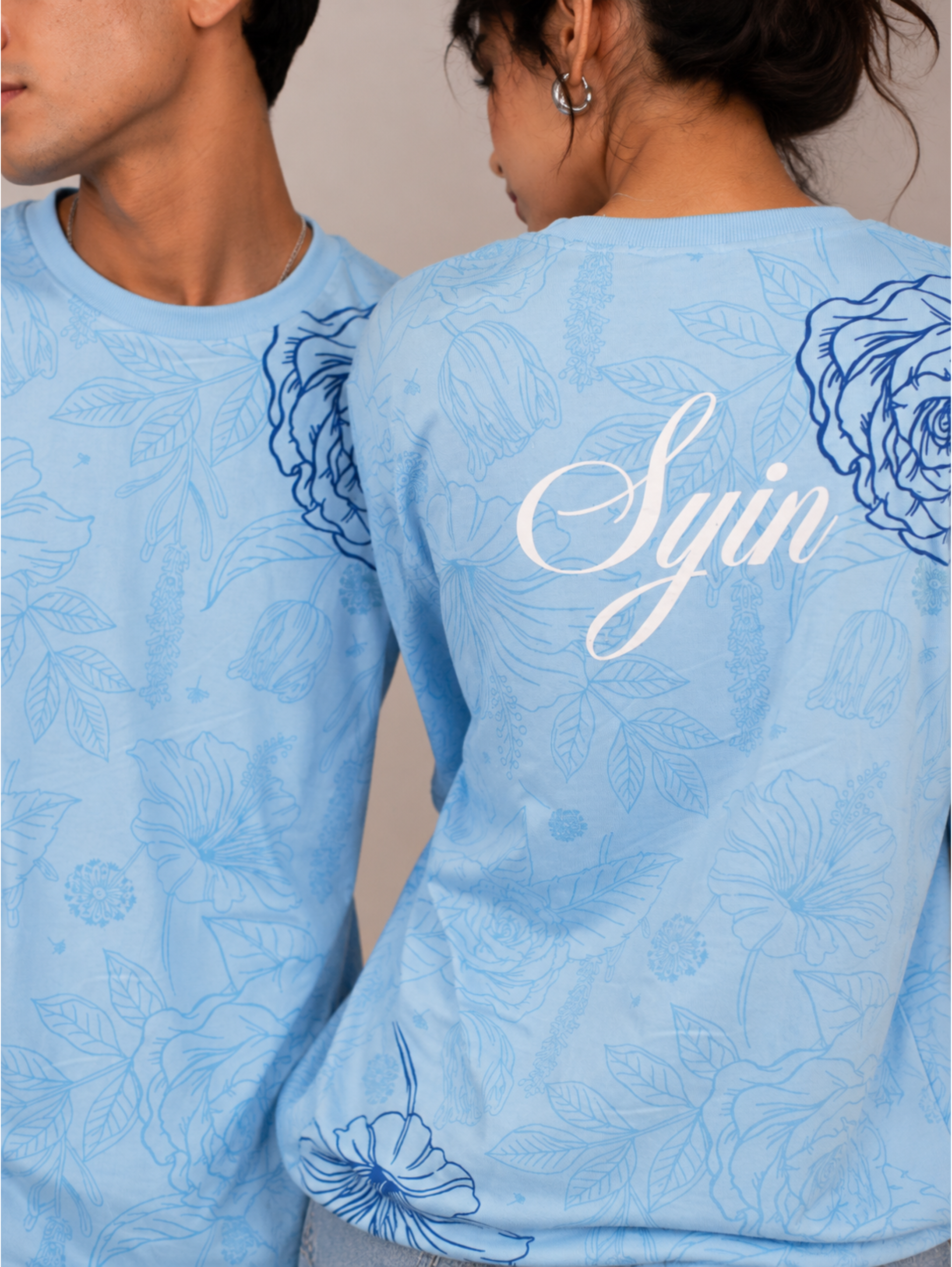 Close-up of the Vita in Blu premium oversized sky blue cotton T-shirt by SYIN & SYRAH showcasing the back signature Syin logo, floral all-over print, premium fabric texture, and high-quality screen printing.